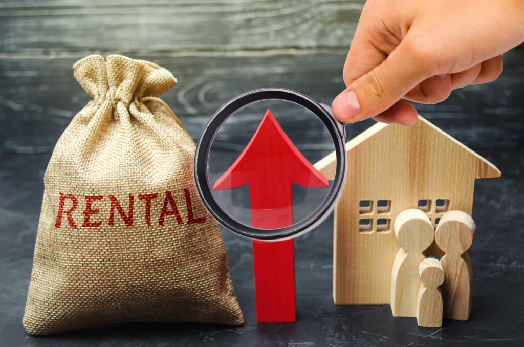 Magnifying glass highlighting rising rental costs next to a model house, family figures, and an upward arrow representing housing affordability