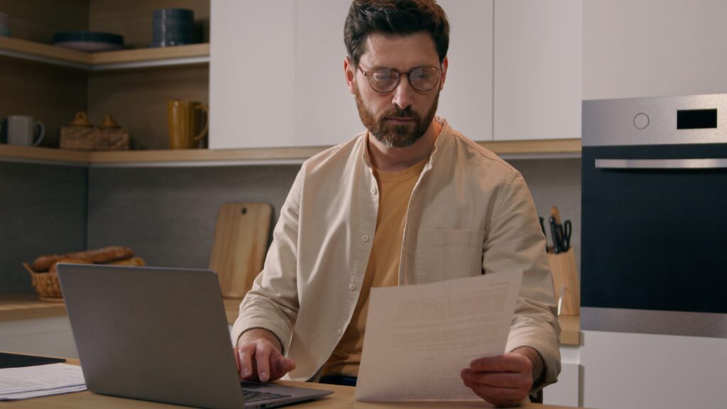 Renter reviewing apartment application paperwork while checking credit information on a laptop.